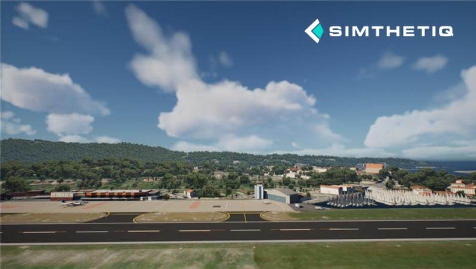 Aerial view of an airport with runways, buildings, and surrounding greenery under a partly cloudy sky.