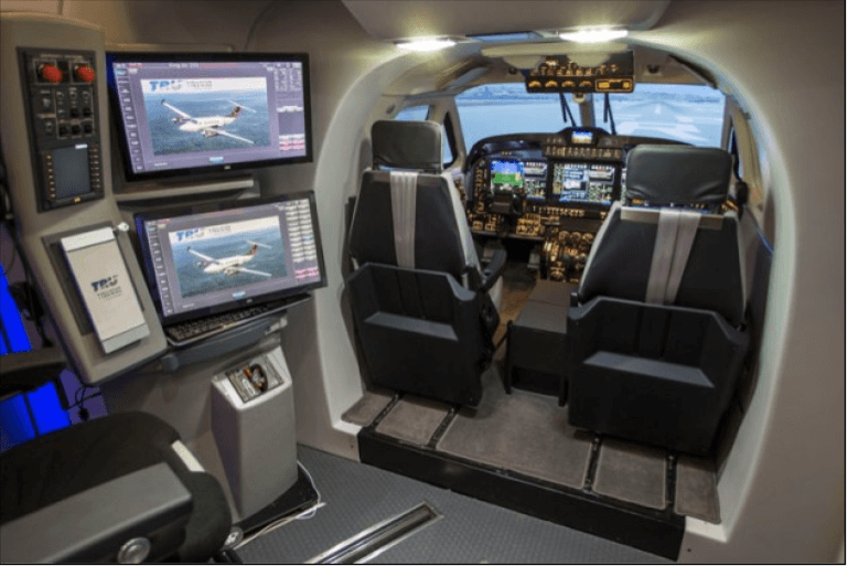 Interior view of a flight simulator cockpit with two seats, multiple screens, and control panels.
