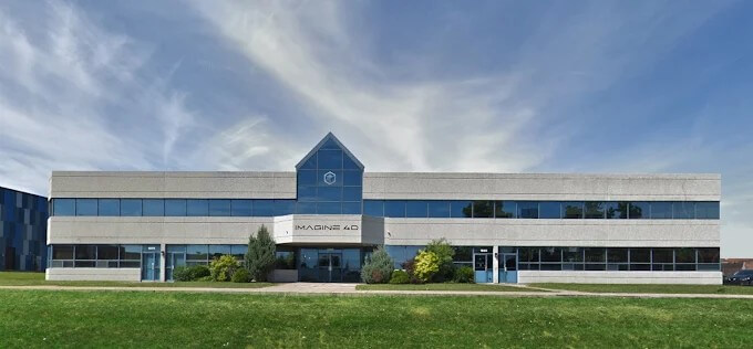 modern two-story building with large windows and a triangular roof, surrounded by green grass and trees.