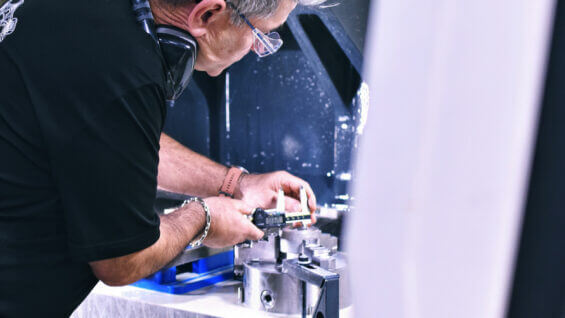 person uses a caliper to measure a metal part in a workshop setting.