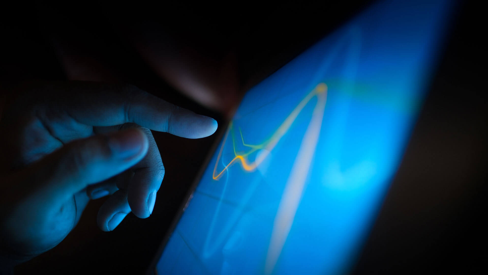 close-up of a hand touching a glowing screen displaying colorful graphs on a dark background.