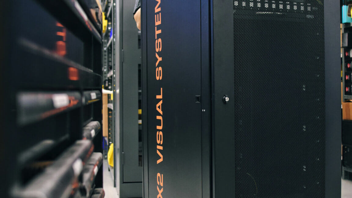 close-up of a black equipment rack labeled "X2 VISUAL SYSTEM" in a storage area with shelves and tools.